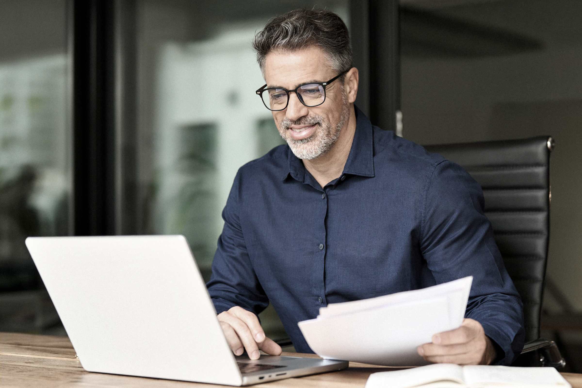 Happy busy young business owner using laptop holding corporate documents in office.